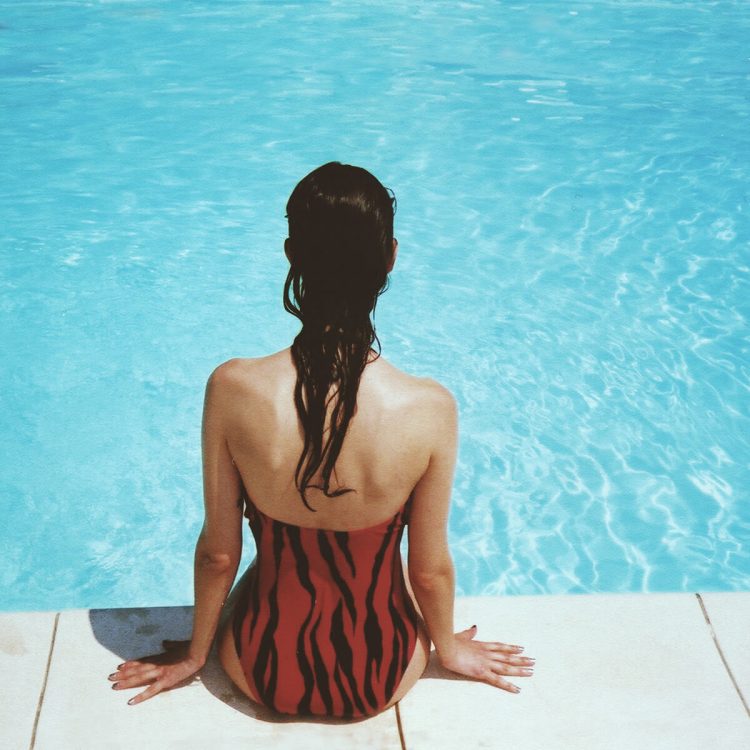 Mujer de espaldas con vestido rojo atigrado y las piernas dentro de la piscina